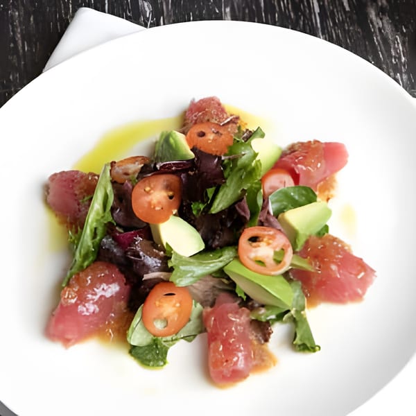Asiana Cafe's tuna tataki salad with mixed greens, avocado, and cherry tomatoes on a white plate.