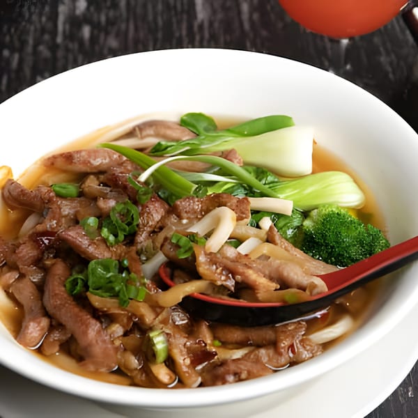 Asiana Cafe's beef noodle soup with bok choy, broccoli, and mushrooms, served with a red spoon.