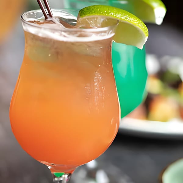 A vibrant orange cocktail with a lime wedge and straws, with a green drink in the background.